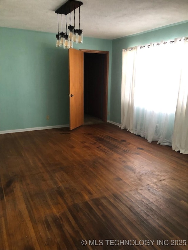 spare room with a notable chandelier and dark wood-type flooring