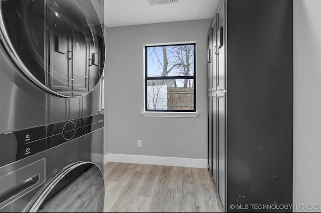 laundry room with stacked washing maching and dryer and light hardwood / wood-style flooring