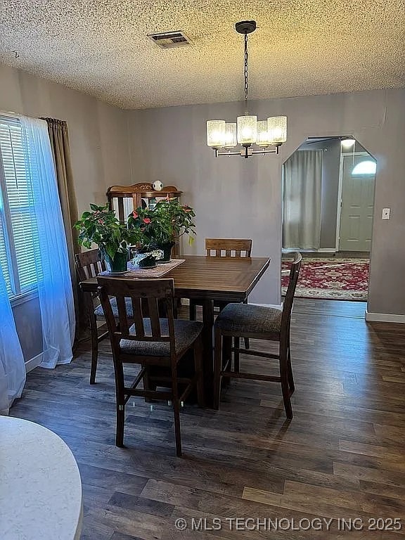 dining space with a textured ceiling, dark hardwood / wood-style flooring, and an inviting chandelier