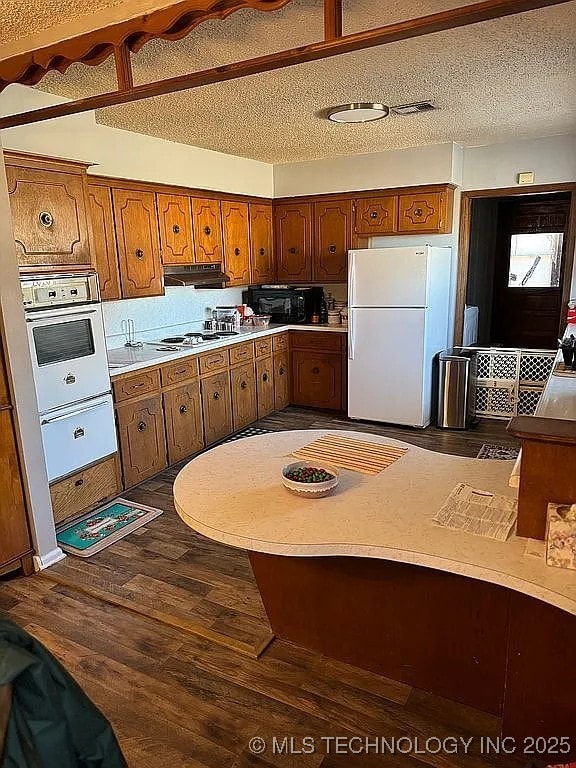 kitchen featuring dark hardwood / wood-style flooring, white appliances, and a textured ceiling