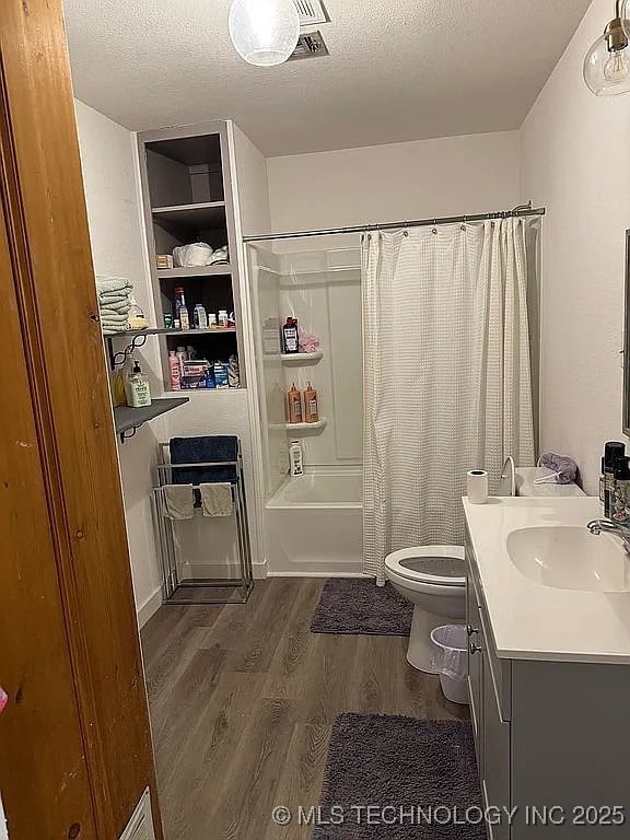 full bathroom featuring a textured ceiling, shower / tub combo, toilet, wood-type flooring, and vanity