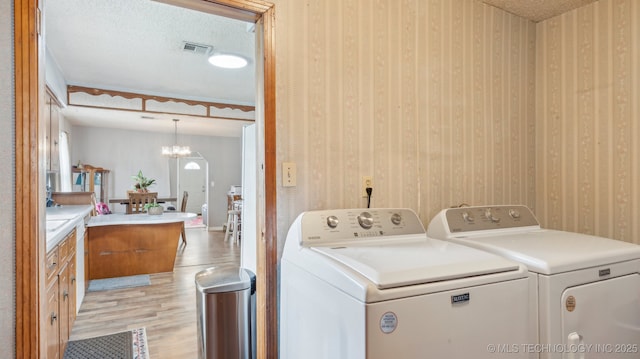 2019 Mckenzie Rd, Pawhuska, OK 74056 - washroom featuring light wood finished floors, washer and dryer, wallpapered walls, a chandelier, and a textured ceiling