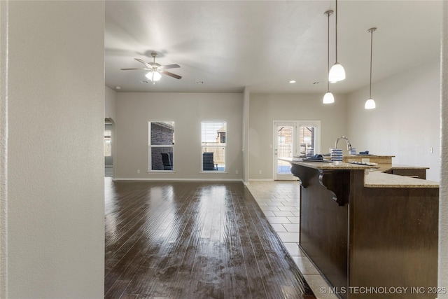 kitchen with an island with sink, ceiling fan, dark hardwood / wood-style flooring, light stone counters, and decorative light fixtures