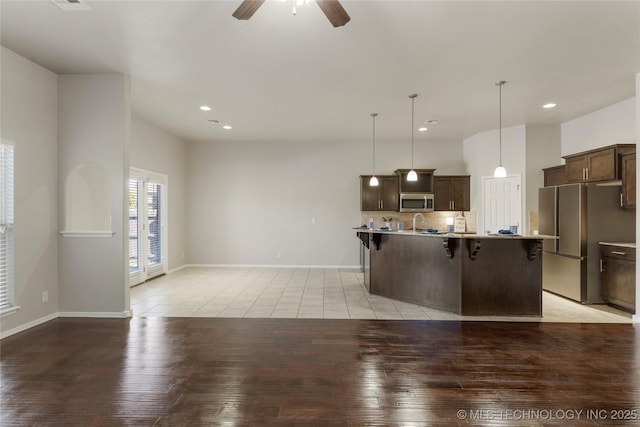 kitchen featuring a center island with sink, a breakfast bar area, appliances with stainless steel finishes, pendant lighting, and dark brown cabinets