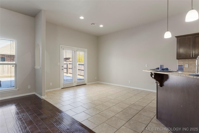 interior space with light tile patterned floors, pendant lighting, a kitchen bar, decorative backsplash, and dark brown cabinets