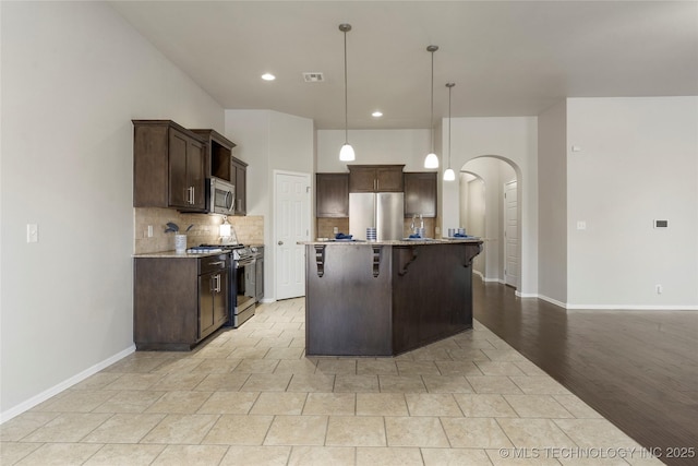 kitchen featuring a breakfast bar area, hanging light fixtures, dark brown cabinetry, a kitchen island with sink, and appliances with stainless steel finishes