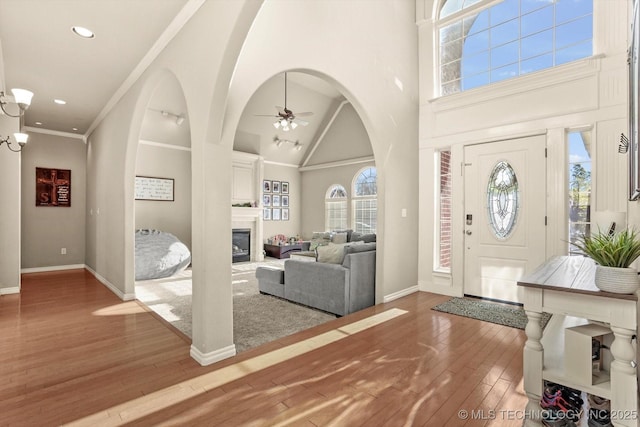 entrance foyer with a large fireplace, hardwood / wood-style flooring, a high ceiling, ornamental molding, and ceiling fan