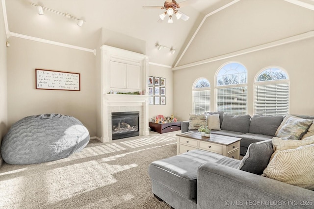 living room with track lighting, high vaulted ceiling, carpet floors, a tiled fireplace, and ceiling fan