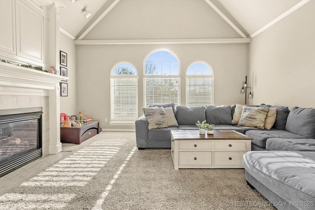 carpeted living room with high vaulted ceiling, a tiled fireplace, and ornamental molding