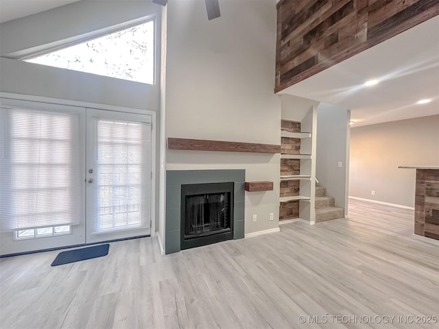 unfurnished living room with a tile fireplace, french doors, light hardwood / wood-style floors, high vaulted ceiling, and plenty of natural light