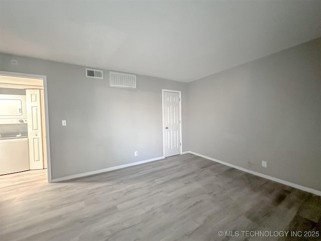 unfurnished room with stacked washer / dryer and wood-type flooring