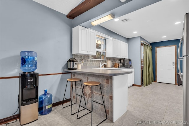 kitchen featuring kitchen peninsula, stainless steel fridge, backsplash, white cabinets, and a kitchen breakfast bar