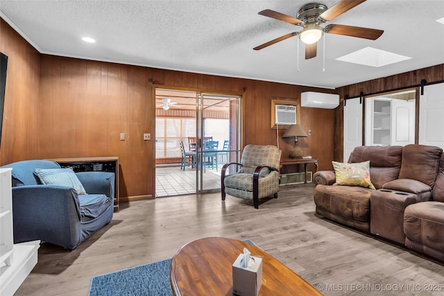 living room with a textured ceiling, a wall unit AC, light hardwood / wood-style floors, wooden walls, and a barn door