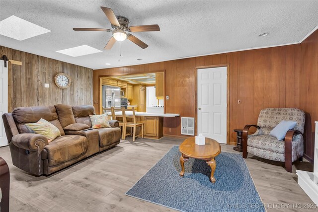 living room featuring wood walls, light wood-type flooring, a barn door, heating unit, and ceiling fan