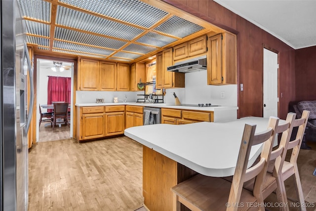 kitchen featuring wood walls, appliances with stainless steel finishes, light wood-type flooring, kitchen peninsula, and ceiling fan