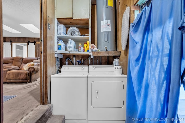 clothes washing area featuring water heater, washer and clothes dryer, a textured ceiling, and a barn door