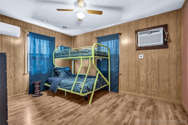 bedroom with a textured ceiling, wood walls, ceiling fan, and a wall mounted air conditioner