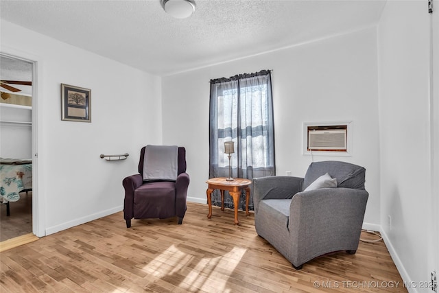 living area with an AC wall unit, ceiling fan, a textured ceiling, and wood-type flooring