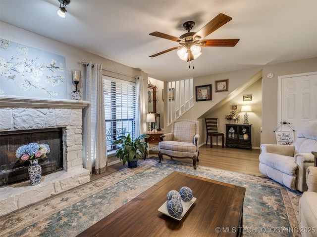 living room featuring ceiling fan, a stone fireplace, and wood-type flooring