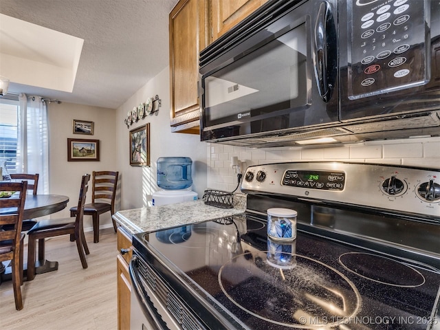 kitchen with stainless steel electric stove, light wood-type flooring, a textured ceiling, stone countertops, and backsplash