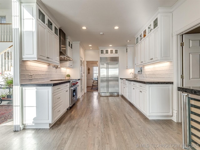 kitchen featuring light hardwood / wood-style floors, white cabinetry, high end appliances, wall chimney exhaust hood, and beverage cooler