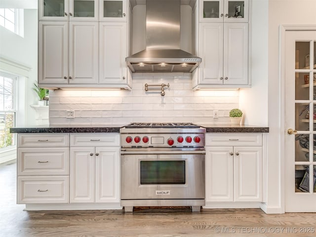 kitchen featuring light hardwood / wood-style floors, white cabinetry, decorative backsplash, wall chimney range hood, and luxury stove