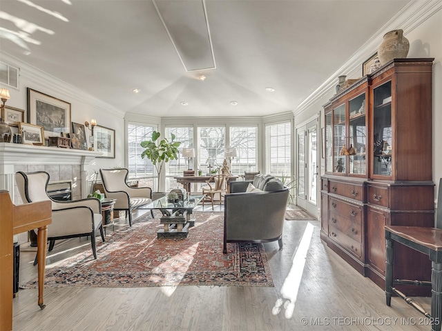 living room featuring a tile fireplace, lofted ceiling, light hardwood / wood-style flooring, and ornamental molding