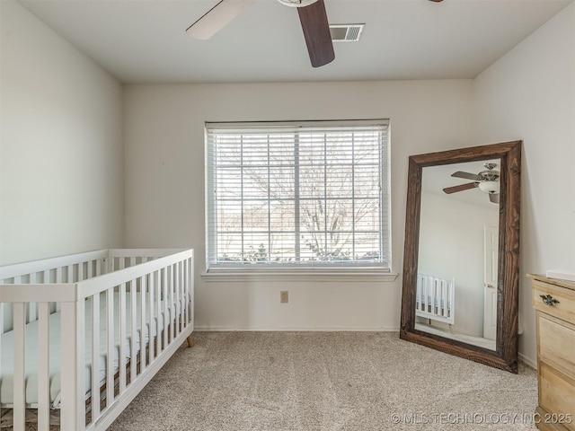 unfurnished bedroom with a crib, light colored carpet, and ceiling fan