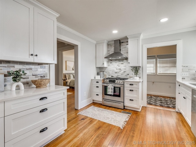 kitchen with appliances with stainless steel finishes, light hardwood / wood-style floors, white cabinetry, wall chimney range hood, and tasteful backsplash