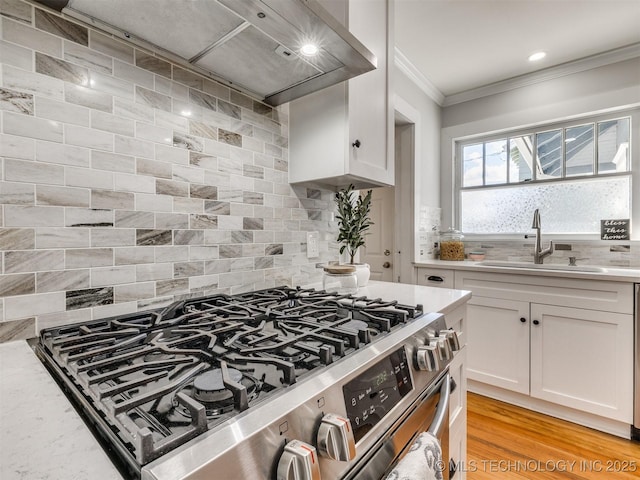 kitchen featuring wall chimney range hood, gas stove, crown molding, white cabinetry, and sink