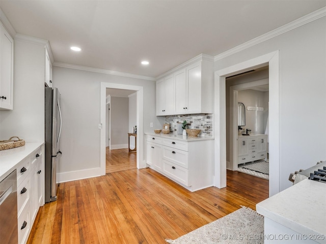 kitchen with light hardwood / wood-style floors, stainless steel appliances, ornamental molding, decorative backsplash, and white cabinets