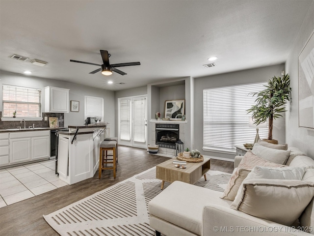 living room with ceiling fan, a tiled fireplace, light hardwood / wood-style floors, and a healthy amount of sunlight