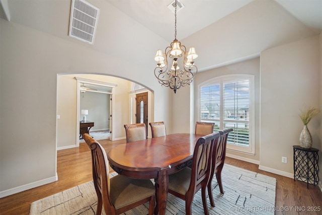 dining area featuring ceiling fan with notable chandelier, hardwood / wood-style flooring, and vaulted ceiling