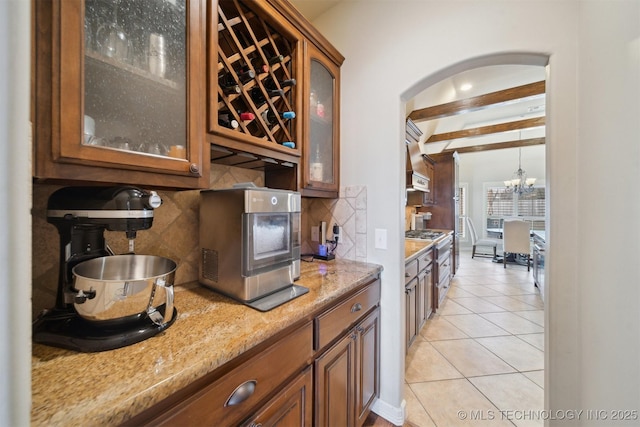 kitchen featuring light stone counters, light tile patterned floors, decorative backsplash, a chandelier, and beam ceiling