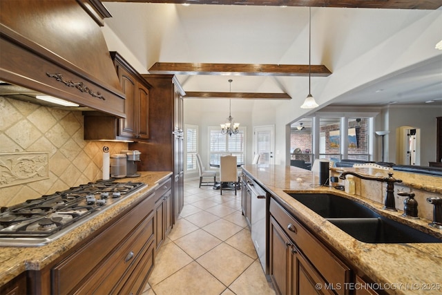 kitchen featuring custom exhaust hood, appliances with stainless steel finishes, light stone counters, sink, and an inviting chandelier