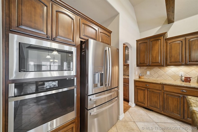 kitchen with stainless steel appliances, vaulted ceiling with beams, light tile patterned floors, light stone counters, and backsplash