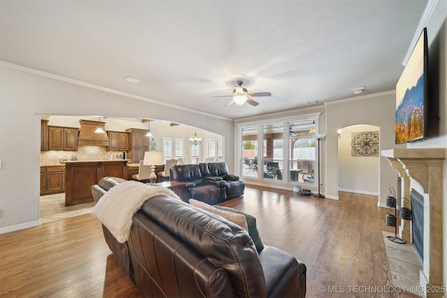 living room with ceiling fan with notable chandelier, ornamental molding, and light wood-type flooring