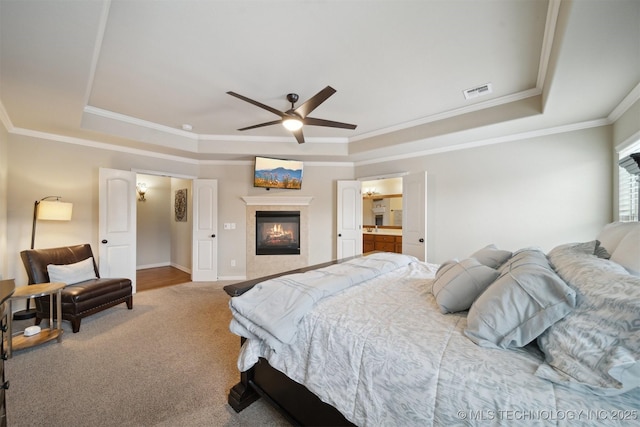 carpeted bedroom featuring ceiling fan, crown molding, a tile fireplace, and a raised ceiling