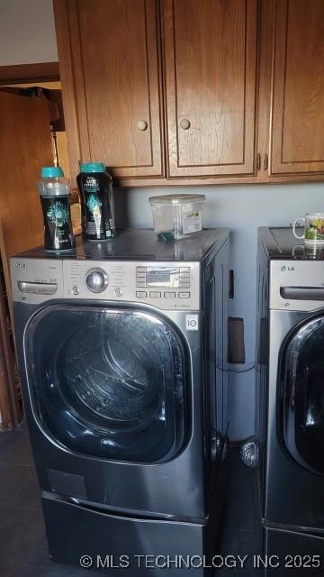 laundry room featuring dark tile patterned floors, washing machine and clothes dryer, and cabinets