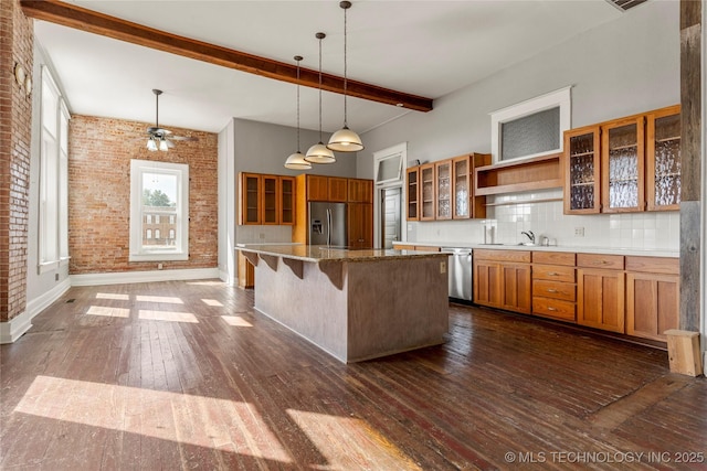 kitchen with a breakfast bar area, appliances with stainless steel finishes, beamed ceiling, a kitchen island, and decorative backsplash