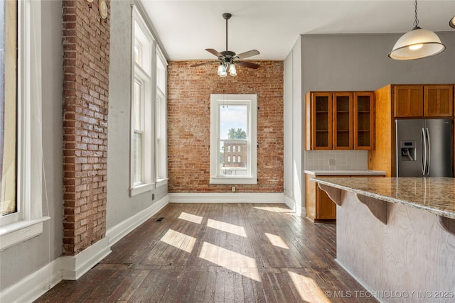 kitchen with a kitchen breakfast bar, tasteful backsplash, stainless steel fridge, brick wall, and dark hardwood / wood-style flooring