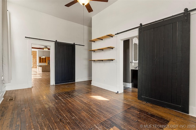 unfurnished living room featuring ceiling fan, a barn door, and dark hardwood / wood-style flooring