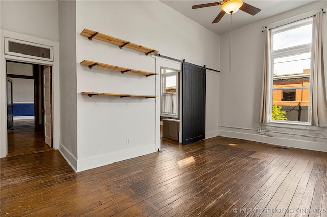 unfurnished bedroom featuring ceiling fan, a barn door, and dark hardwood / wood-style floors