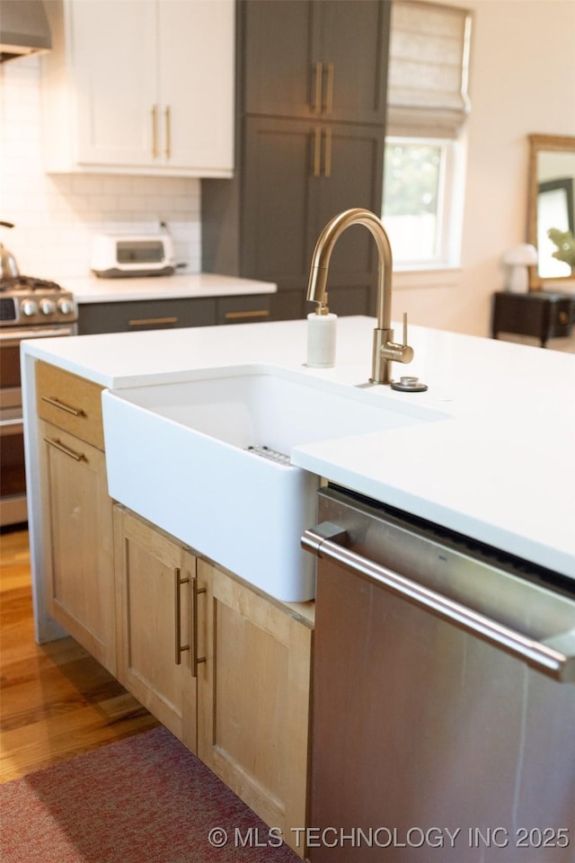 kitchen featuring range hood, backsplash, appliances with stainless steel finishes, wood-type flooring, and light brown cabinets