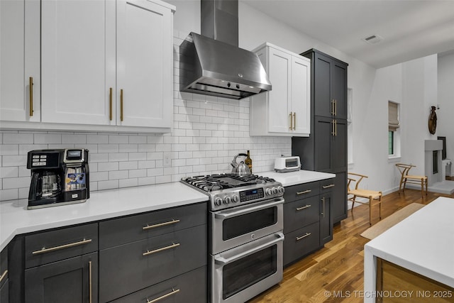 kitchen featuring white cabinets, light wood-type flooring, backsplash, wall chimney range hood, and double oven range