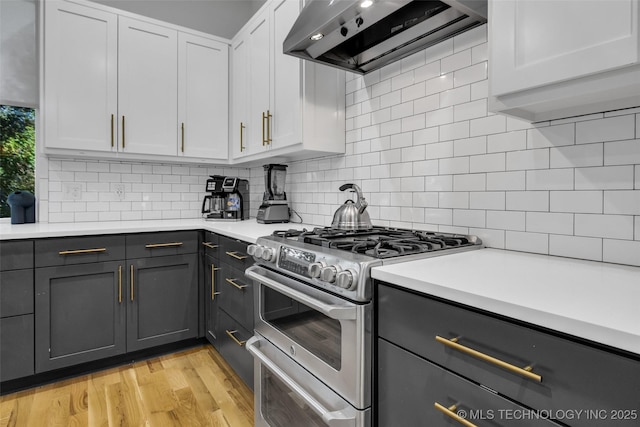 kitchen featuring range with two ovens, white cabinets, wall chimney range hood, and backsplash