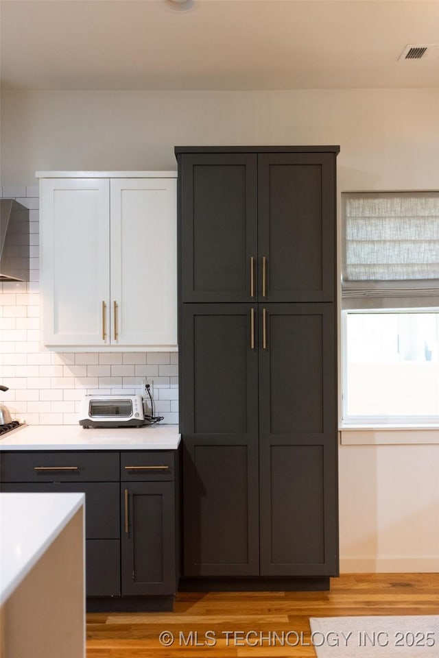 kitchen featuring cooktop, light hardwood / wood-style flooring, tasteful backsplash, and white cabinetry