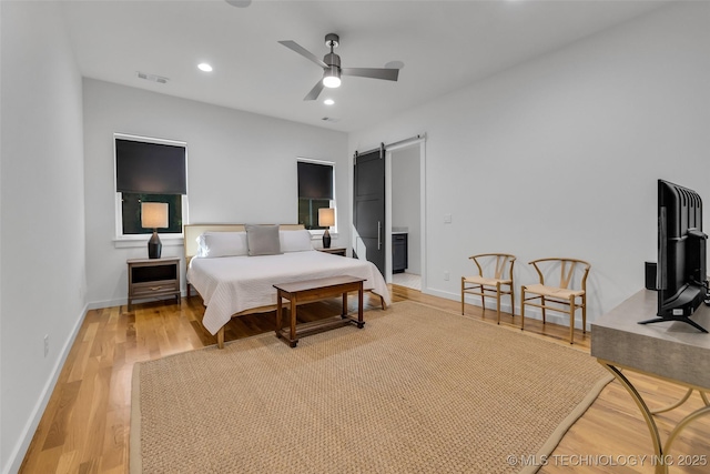 bedroom with light wood-type flooring, ceiling fan, and a barn door