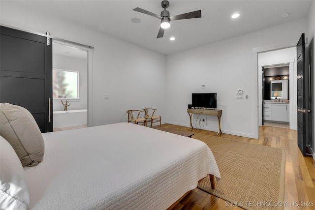 bedroom with ceiling fan, ensuite bath, light hardwood / wood-style flooring, and a barn door