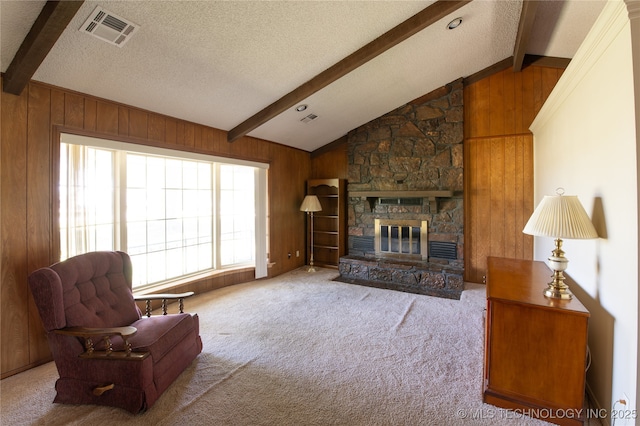 carpeted living room featuring wood walls, a textured ceiling, vaulted ceiling with beams, and a stone fireplace